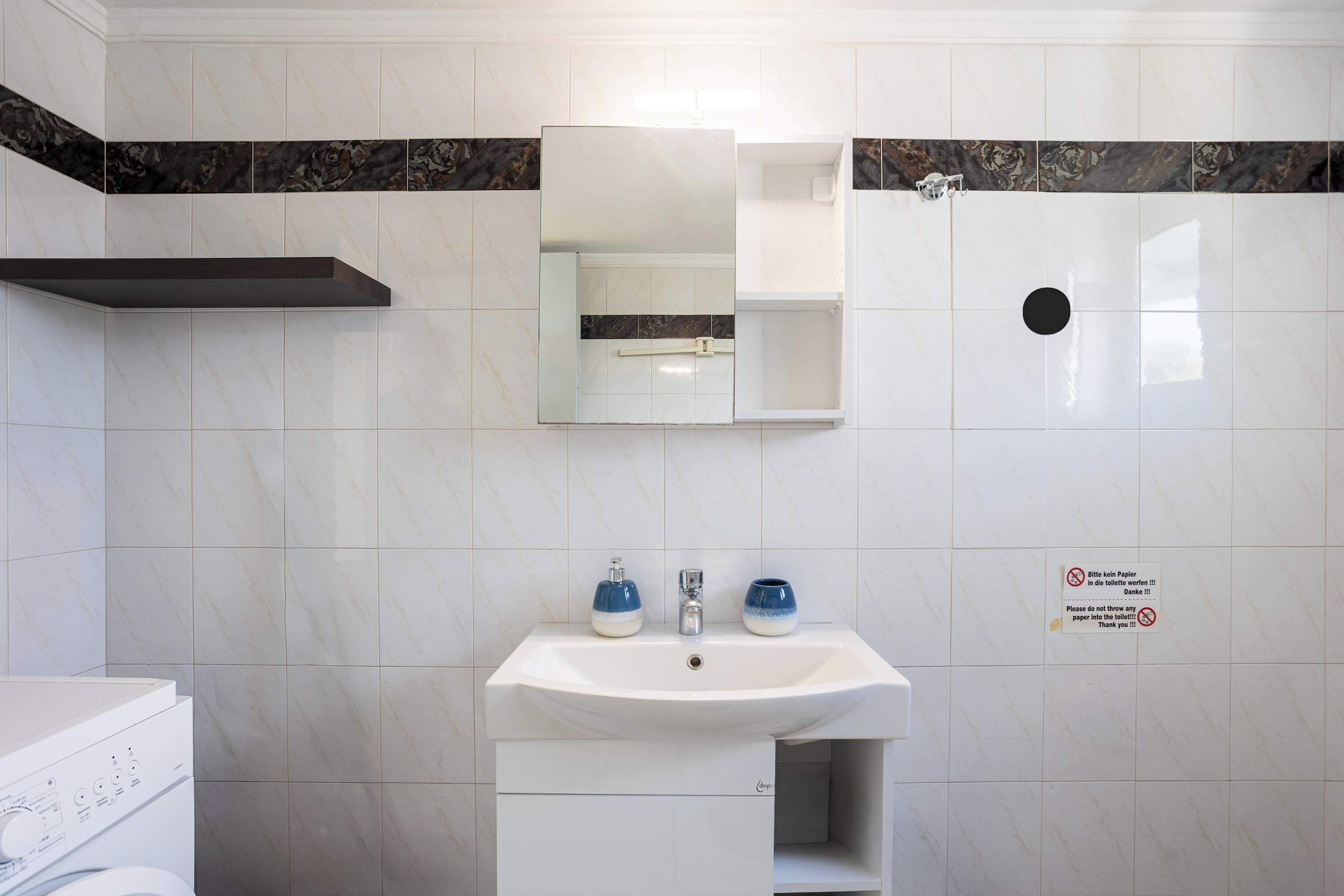Et badeværelse med en hvid vask, to blå sæbedispensere, et spejl og et toilet.