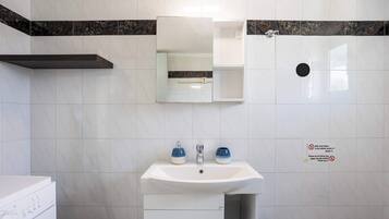 Et badeværelse med en hvid vask, to blå sæbedispensere, et spejl og et toilet.