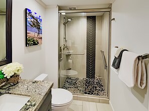 Une salle de bain moderne dotée d’une douche à parois de verre, d’un comptoir en marbre, de toilettes blanches et d’un lavabo fixé au mur.
