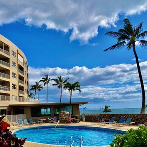 Une piscine d’hôtel offrant une vue dégagée sur l’océan, les palmiers et un immeuble à plusieurs étages doté de balcons.