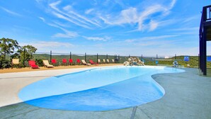 A swimming pool with a curved edge, surrounded by red and beige lounge chairs, and a fenced area with a view of the landscape. - 51-05 Lake view unit Close to SDC Indoor/Outdoor pools (Branson)