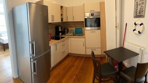 A compact kitchen with a stainless steel refrigerator, a built-in oven, and a small dining area with two chairs. - Vacation apartment Villa am Meer - Experience Stralsund (Stralsund)