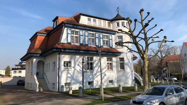 A two-story building with a traditional architectural style, featuring a red-tiled roof and white walls with blue window frames. - Vacation apartment Villa am Meer - Experience Stralsund (Stralsund)