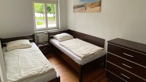 A bedroom with two single beds, a wooden dresser, a radiator, and a window with a view of greenery. - Vacation apartment Villa am Meer - Experience Stralsund (Stralsund)