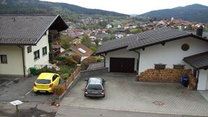 A residential area with a paved driveway, two cars parked, and a building with a tiled roof.