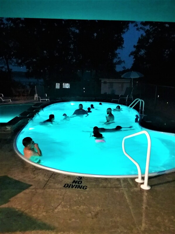 A swimming pool with people in it, surrounded by lounge chairs and umbrellas.