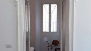 A narrow hallway with a bed, a chair, and a window. - Flatty Alassio - Three Dots (Alassio)