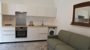 A compact kitchen with white cabinets, a built-in oven, a washing machine, and a kettle on the countertop. - Flatty Alassio - Three Dots (Alassio)
