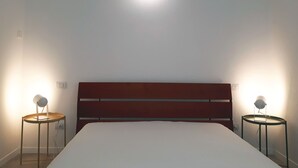 A bedroom with a wooden headboard, a bed, two bedside tables with lamps, and a ceiling light. - Flatty Alassio - Three Dots (Alassio)