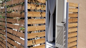 Una cerca de madera con plantas trepadoras, un ventanal corredero y un patio con baldosas.
