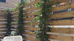 A wooden fence with climbing plants, a white plastic chair, and a round table with a green base. - Flatty Alassio - Three Dots (Alassio)
