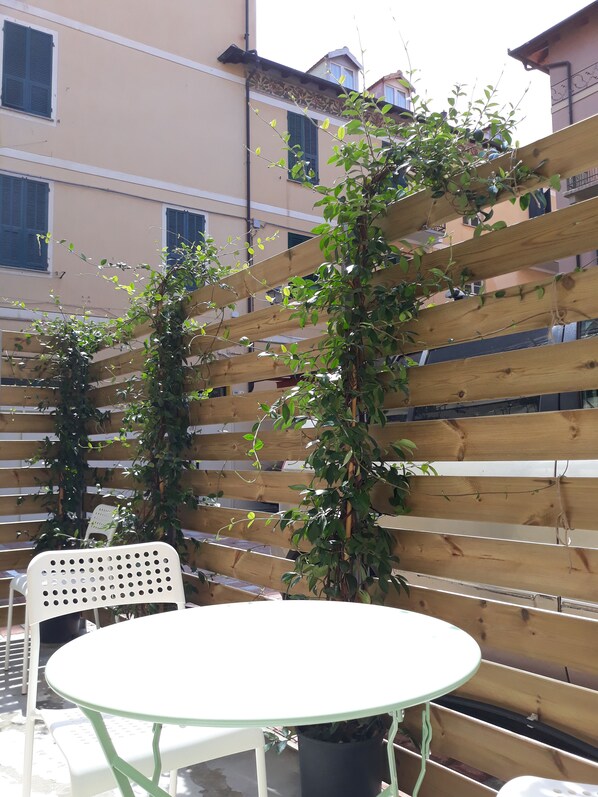 Una cerca de madera con plantas trepadoras, una silla de plástico blanca y una mesa redonda con base verde.