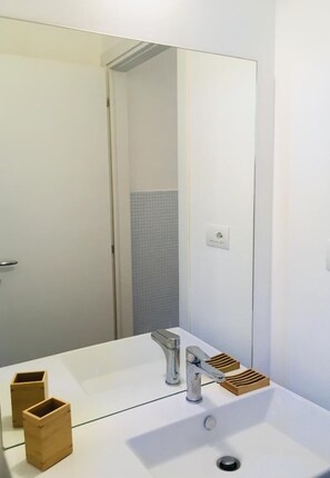 Un baño moderno con un lavabo blanco, un espejo y una puerta.