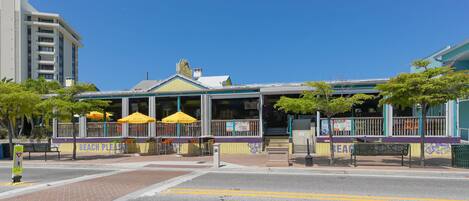 A beachside restaurant with outdoor seating, a clear sky, and a pedestrian crossing.