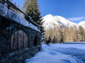 A stone building with wooden doors and a snow-covered landscape with a mountain in the background. - Flatty La Thuile - Little Fish (La Thuile)