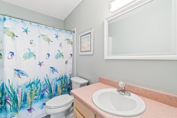 Un baño con cortina de ducha de tortuga marina, un inodoro blanco y un lavamanos con encimera rosa.