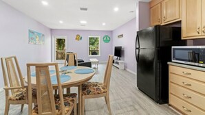 Une cuisine moderne avec des meubles en bois, un réfrigérateur noir et un four à micro-ondes. On y trouve également un coin repas avec une table ronde et des chaises.