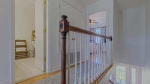 A staircase with a wooden handrail and white balusters, leading to a room with a ceiling fan and a view of the outdoors. - Cozy Coastal Beach Villa (Pensacola Beach)