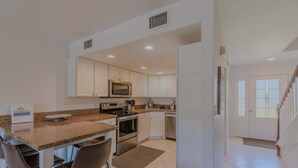 A modern kitchen with white cabinets, stainless steel appliances, and a granite countertop. - Cozy Coastal Beach Villa (Pensacola Beach)