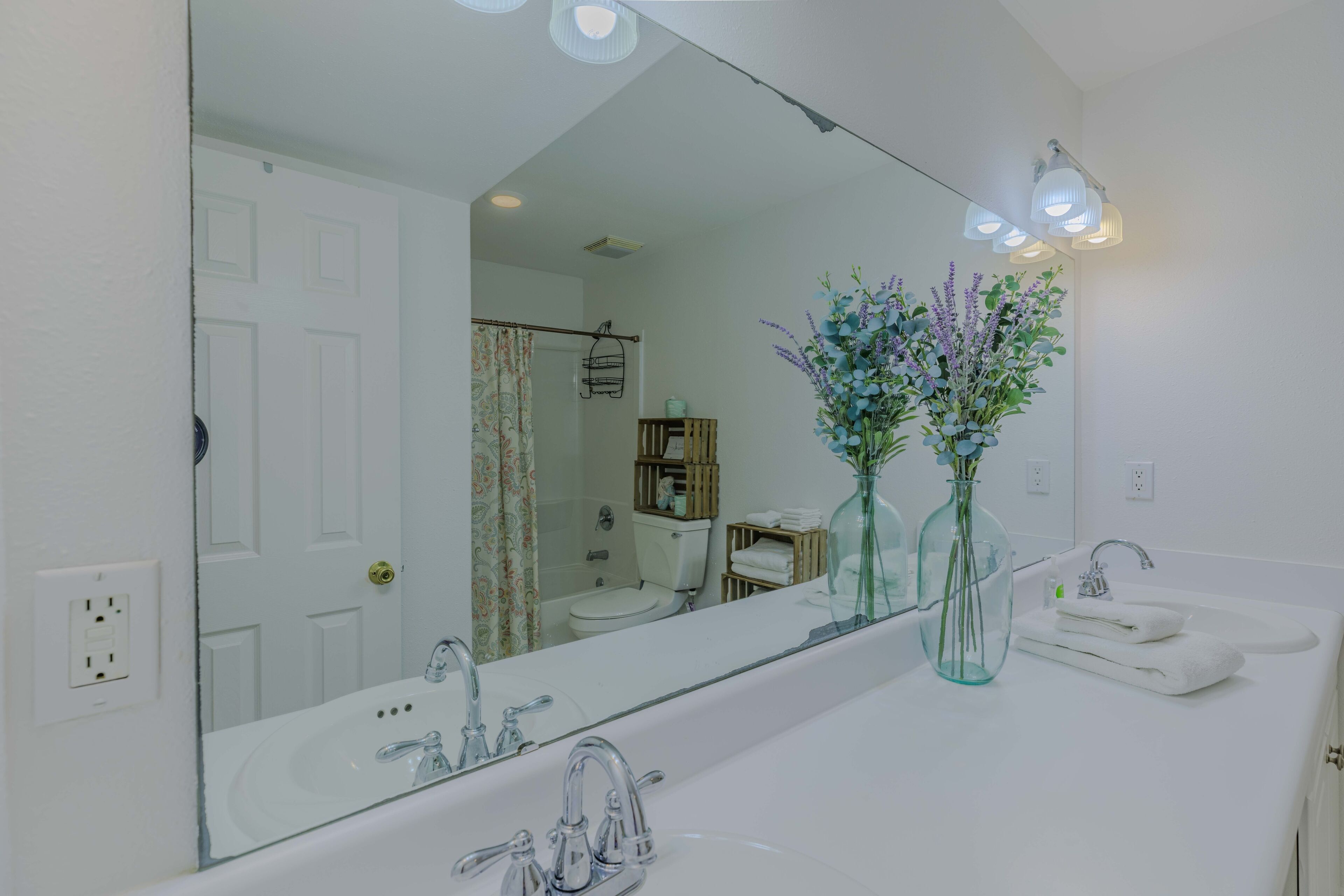 Un baño con un espejo grande, un lavabo blanco y dos jarrones con flores.