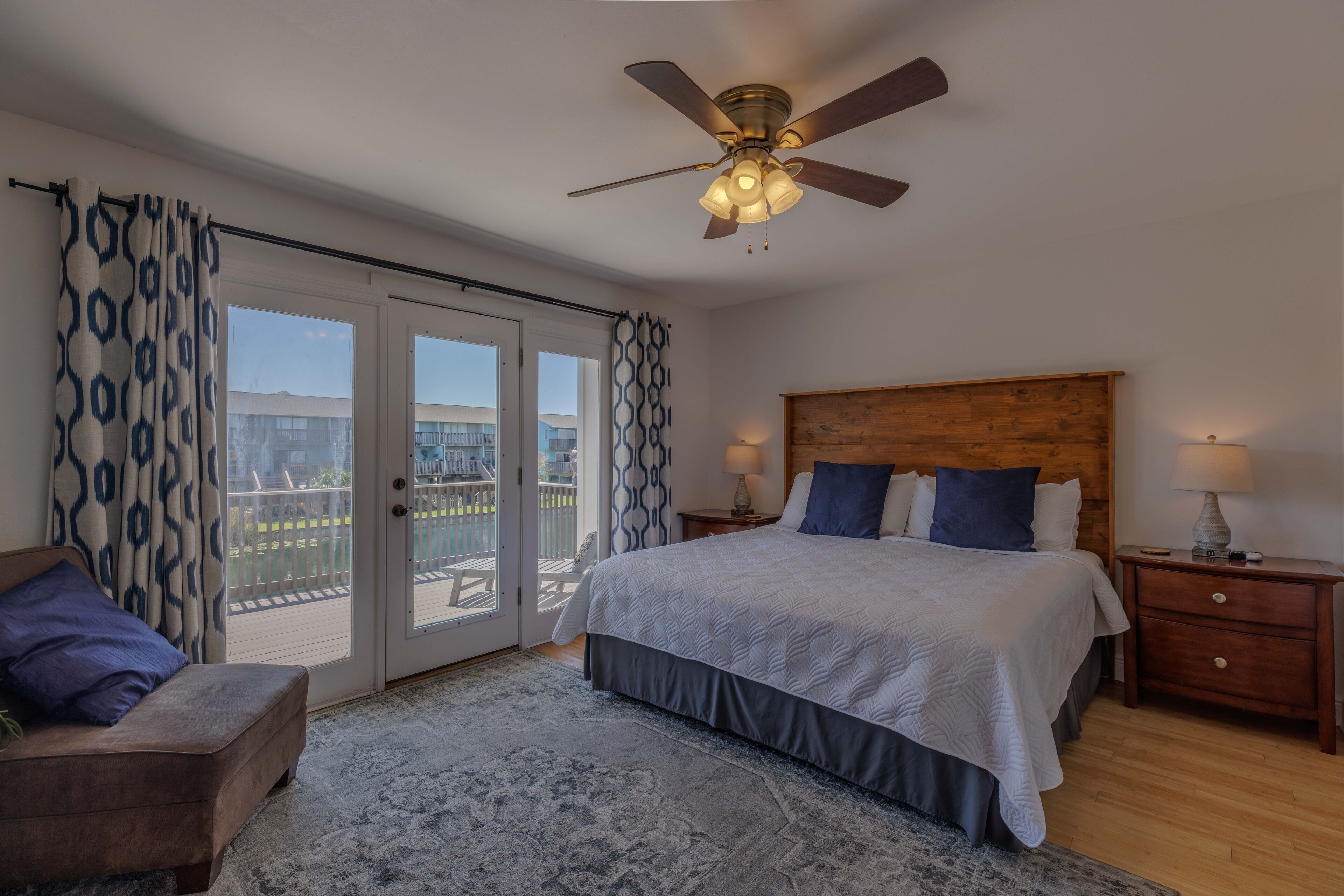 Ein Schlafzimmer mit Bett, Nachttischen, einem Deckenventilator und Blick durch Glastüren.