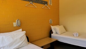 A hotel room with two single beds, each with white linens and pillows, a wooden bench, and two wall-mounted light fixtures.