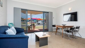 A modern living room with a blue sofa, a wooden coffee table, and a dining area with a table and chairs. - Windsurfer Beach Chalet  2 - No Frills holiday vibe (Lancelin)