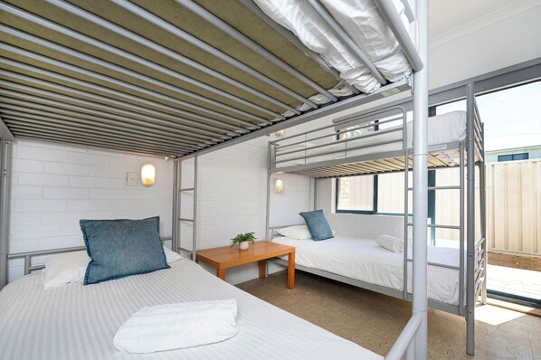 A bunk bed room with a wooden table, white bedding, and a view through a window. - Windsurfer Beach Chalet 2 - No Frills holiday vibe (Lancelin)