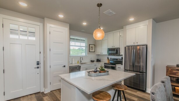 A modern kitchen with white cabinetry, stainless steel appliances, and a central island with stools. - Lake front Condo 2BD/2BA w/ pool, hot tub, fire pit, gas grills, gym, & laundry. (Graford)