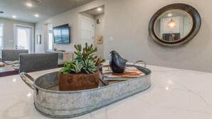 A modern living room with a marble coffee table, a potted plant, and a decorative bird sculpture. - Lake front Condo 2BD/2BA w/ pool, hot tub, fire pit, gas grills, gym, & laundry. (Graford)