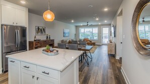 A modern kitchen with white cabinetry, a stainless steel refrigerator, and a marble island. - Lake front Condo 2BD/2BA w/ pool, hot tub, fire pit, gas grills, gym, & laundry. (Graford)