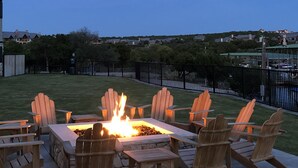 A backyard with a fire pit and Adirondack chairs, surrounded by a stone wall and a black fence. - Lake front Condo 2BD/2BA w/ pool, hot tub, fire pit, gas grills, gym, & laundry. (Graford)