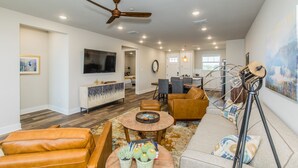 A spacious living room with leather sofas, a coffee table, and a dining area with chairs and a table. - Lake front Condo 2BD/2BA w/ pool, hot tub, fire pit, gas grills, gym, & laundry. (Graford)