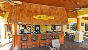 Uma área de bar com teto de palha, cadeiras de bambu e um balcão com uma placa que diz "LANDSHARK Lager".