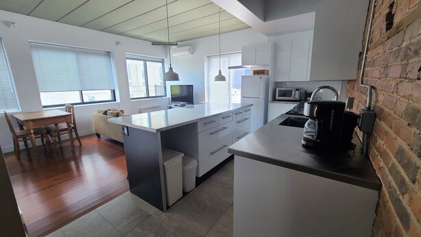 A modern kitchen with a central island, white cabinetry, and a brick accent wall. - Huge terrace - Downtown condo - Free parking - Near Old Port (Montréal)