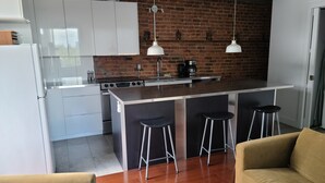 A modern kitchen with white cabinets, a brick wall, a central island with stools, and a coffee machine. - Huge terrace - Downtown condo - Free parking - Near Old Port (Montréal)
