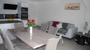 A modern kitchen with a dining area, a grey sofa, and a painting on the wall. - Appartement T3 Avec Terrasse et Accès Direct à la Plage (Fréhel)