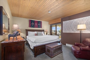 Habitación de hotel con techo de madera, una cama grande, un sillón de cuero rojo y vistas a través de un ventanal.