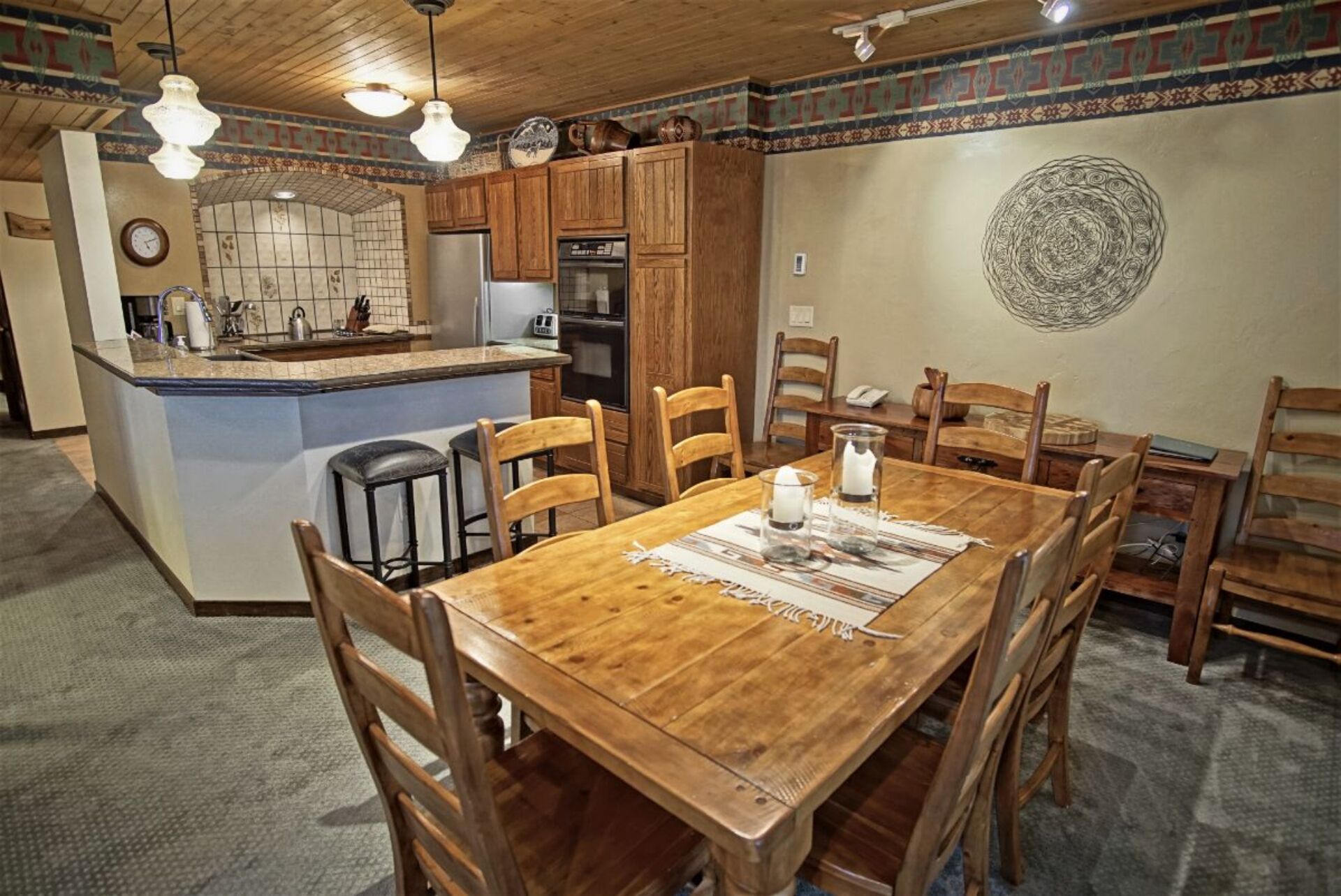 A wooden dining table with chairs, a kitchen island with a sink and appliances, and a decorative wall pattern.