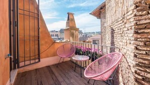 A balcony with a wooden floor, a metal gate, and two pink chairs.