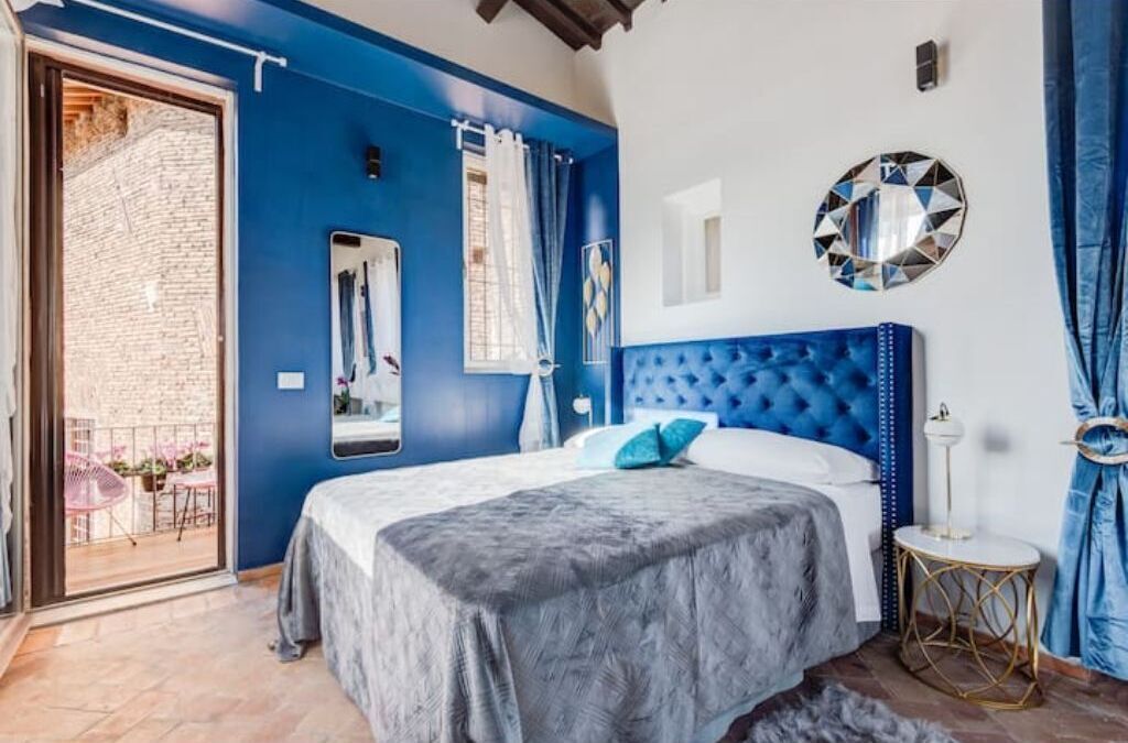 Camera da letto con una parete azzurra, una testiera imbottita, un grande specchio e un elemento decorativo rotondo a parete.