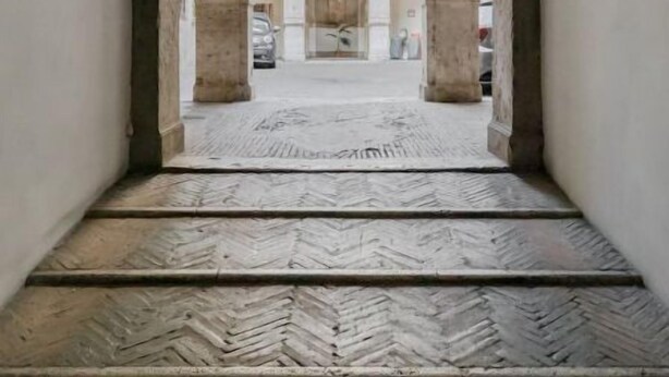 A corridor with a herringbone-patterned floor, arched ceilings, and a hanging light fixture.