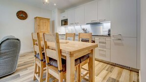 A modern kitchen with white cabinets, a wooden dining table, and a grey armchair. - Lapia 3 : New 2 bedrooms with garden by the centre in a tranquil location (MORZINE)
