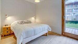 A bedroom with a bed, bedside table, and a window with a view of a balcony. - Lapia 3 : New 2 bedrooms with garden by the centre in a tranquil location (MORZINE)