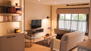 Uma sala de estar com sofá, mesa de centro, televisão e estante de livros.