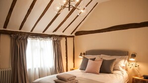 Quarto com cama, mesa de cabeceira, luminária e janela com cortinas.