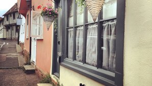 Uma rua estreita com edifícios tradicionais, um deles com uma janela decorada com cestos de flores penduradas.