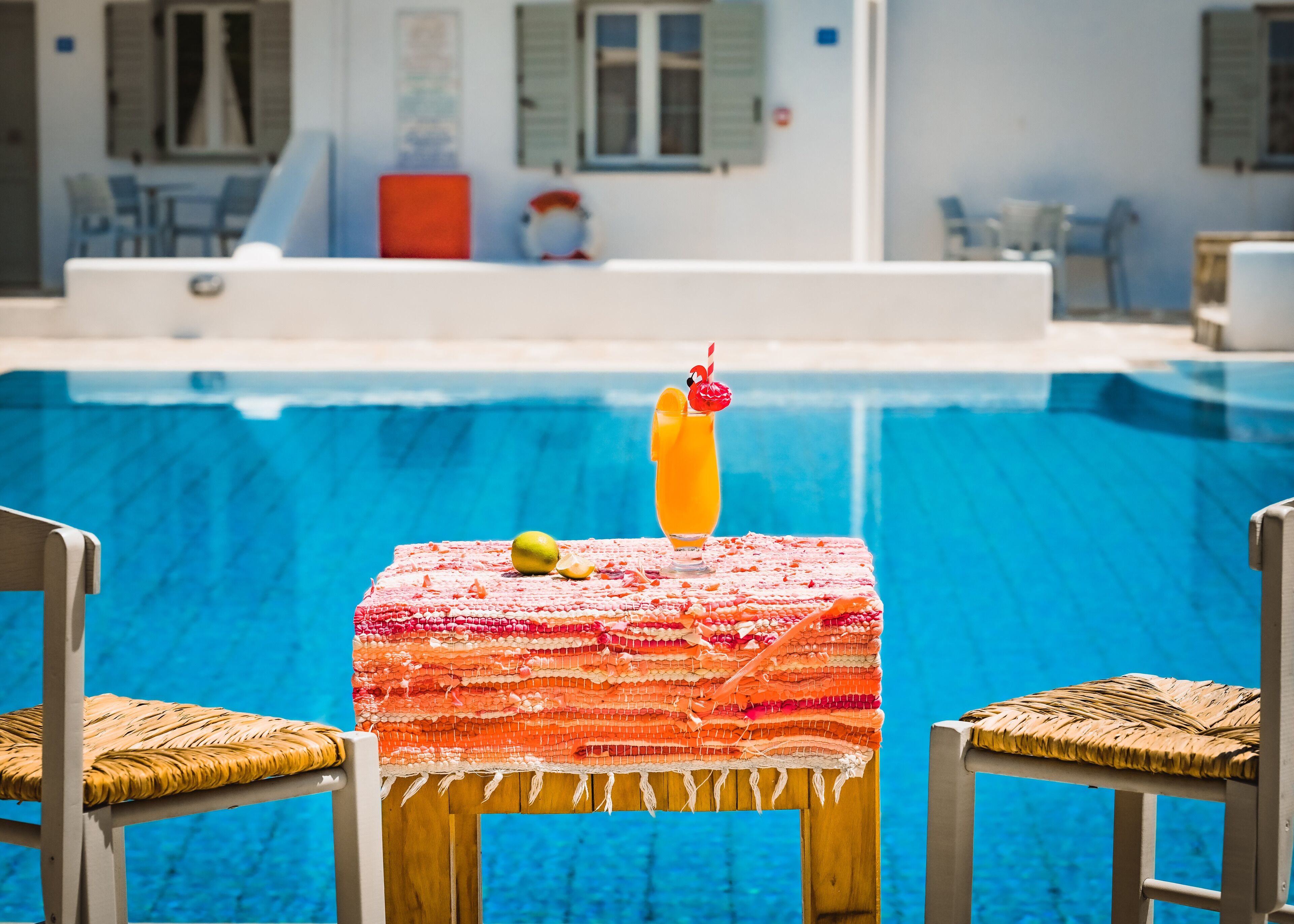 A poolside table with a drink and fruit, surrounded by wicker chairs.