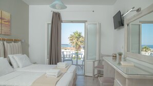 A hotel room with a bed, a desk, a chair, a TV, and a balcony with a view of the sea and palm trees. - Summer Shades (Paros)