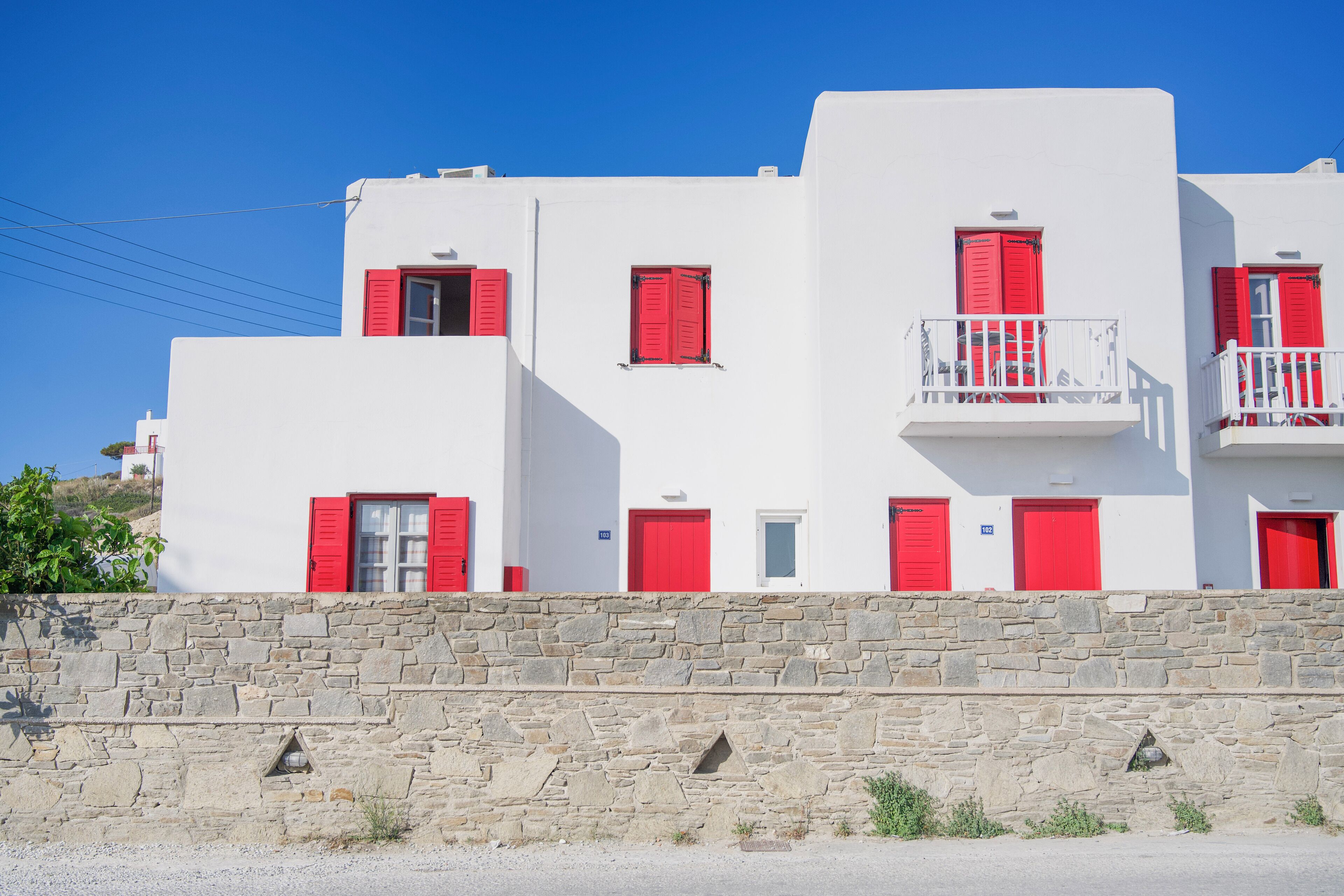 Un bâtiment blanc avec des volets rouges et un mur de pierre à l’avant.